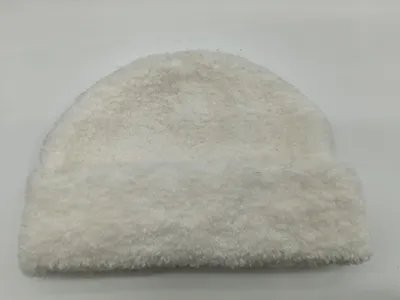 Cremefarbene Plüschmütze aus Sherpa-Fleece mit lockiger Teddystruktur, auf hellem Hintergrund liegend – flauschiges Winteraccessoire