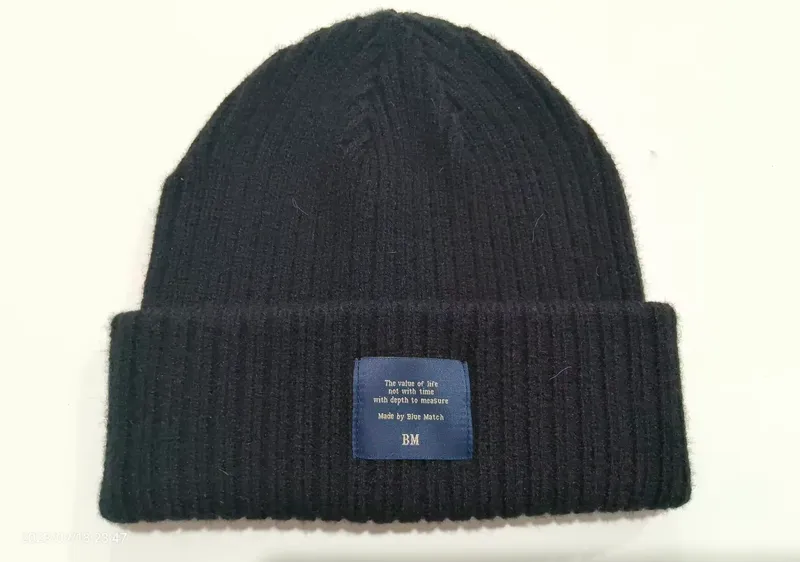 Schwarze gerippte Wintermütze mit breiter Umschlagkrempe und blau gewebtem Label-Patch auf weißem Hintergrund