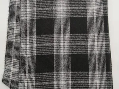 Zusammengelegte schwarz-weiße Tartan-Karierwolldecke aus gewebtem Stoff mit geknoteten Fransenenden auf weißem Hintergrund