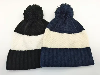 Zwei Strick-Bommel-Beanies in Schwarz-Weiß und Marine-Weiß Streifenmuster nebeneinander auf weißem Hintergrund