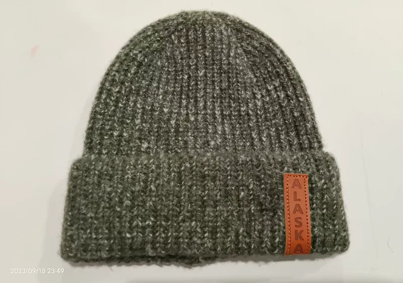 Olivgrüne Wintermütze aus dicker Rippenstrickware mit umgeschlagenem Bund und braunem Leder-Aufnäher, Studioaufnahme