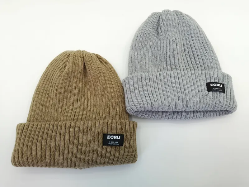 Zwei gerippte Umschlag-Beanies in Khaki und Hellgrau nebeneinander, mit schwarzem Webklabel am Umschlag