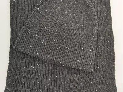 Hellgraue Strickmütze mit Rippmuster und passender Schal aus meliertem Garn auf weißem Untergrund