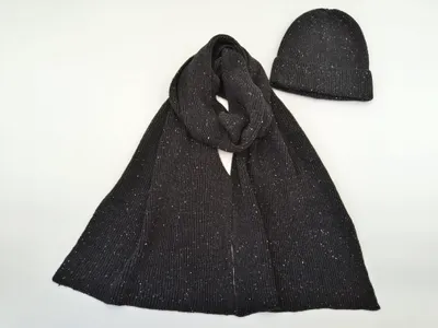 Anthrazitfarbener Rippstrickschal locker drapiert neben passender Beanie-Mütze mit weißem Fleckenmuster
