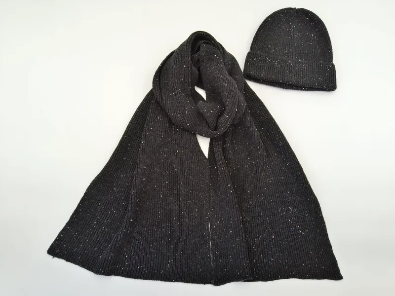 Anthrazitfarbener Rippstrickschal locker drapiert neben passender Beanie-Mütze mit weißem Fleckenmuster