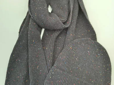 Grauer Rippstrickschal und passende Beanie-Mütze mit bunten Farbsprenkeln auf weißer Fläche