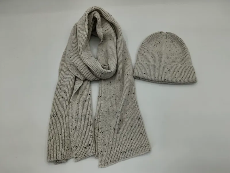 Hellgrauer Rippstrickschal und passende Beanie mit dunklem Sprenkel-Muster nebeneinander auf weißem Hintergrund
