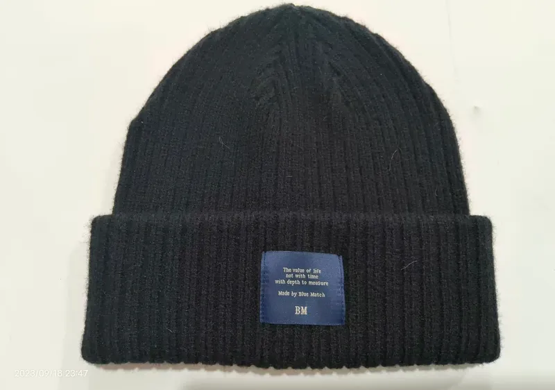 Strukturierte schwarze Strickmütze mit gefaltetem Bündchen und gewebtem Markenpatch auf dem Umschlag, Detailaufnahme