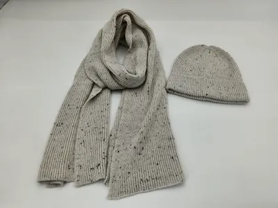 Hellgrauer Rippstrickschal mit dunklem Fleckenmuster und dazu passende Strickmütze auf weißer Fläche
