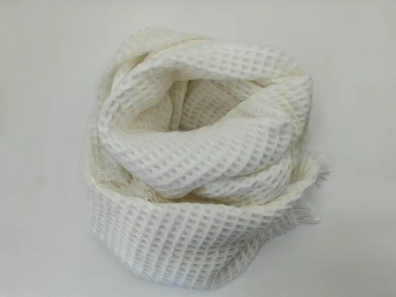 Weißer Schal in Waffeloptik aufgerollt auf heller Fläche mit sichtbaren Fransen und offenem Strickmuster