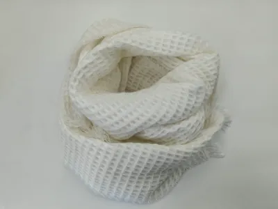 Weißer Schal in Waffeloptik aufgerollt auf heller Fläche mit sichtbaren Fransen und offenem Strickmuster