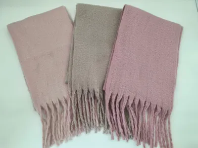 Drei gefaltete Bouclé-Schals mit Fransen in den Farben Altrosa, Taupe und Mauve auf weißer Unterlage