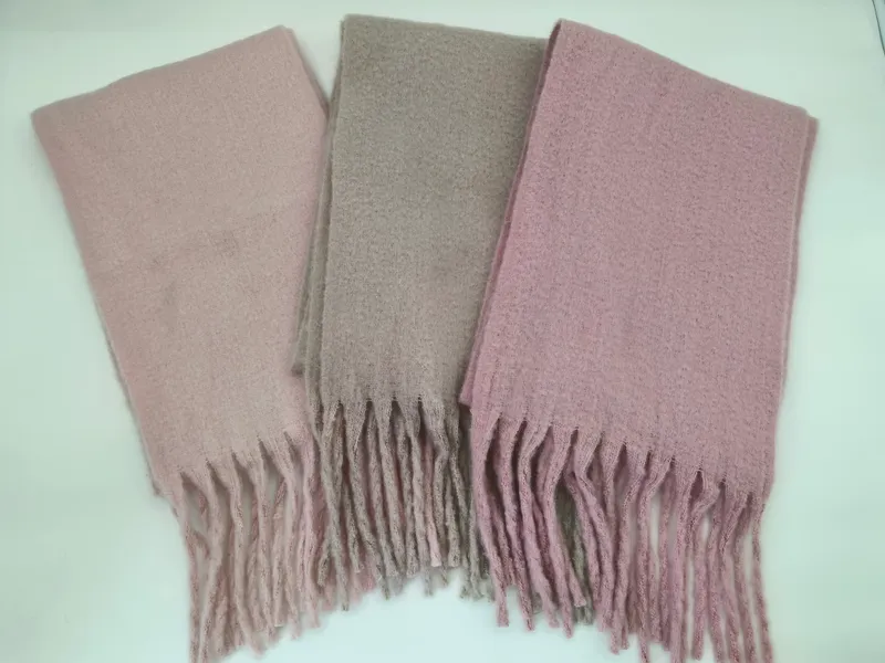 Drei gefaltete Bouclé-Schals mit Fransen in den Farben Altrosa, Taupe und Mauve auf weißer Unterlage