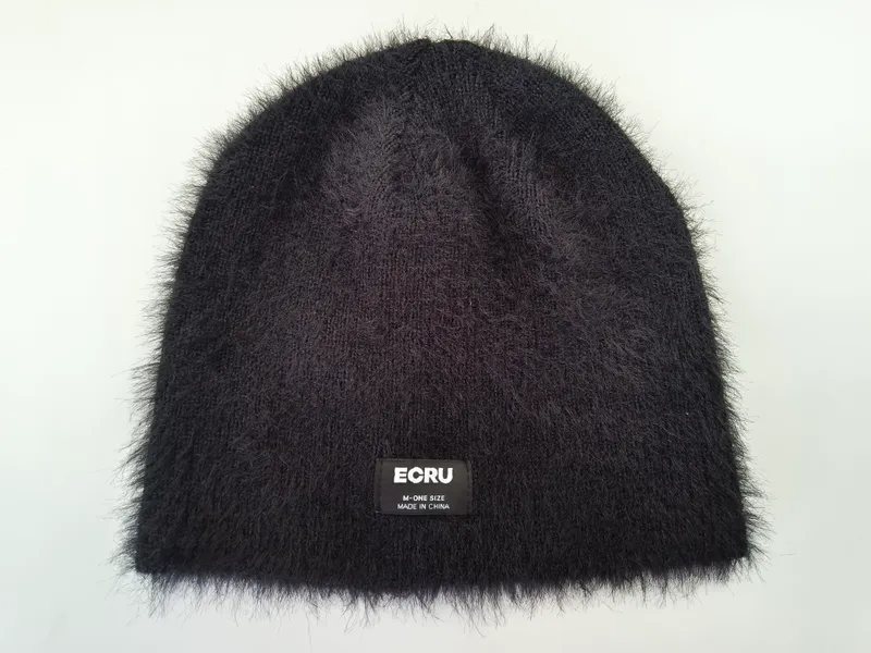 Schwarze Flauschwollmütze mit dichtem, samtartigem Strickflor und aufgenähtem Markenlabel, Draufsicht auf weißem Hintergrund