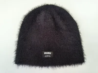 Schwarze Flauschwollmütze mit dichtem, samtartigem Strickflor und aufgenähtem Markenlabel, Draufsicht auf weißem Hintergrund