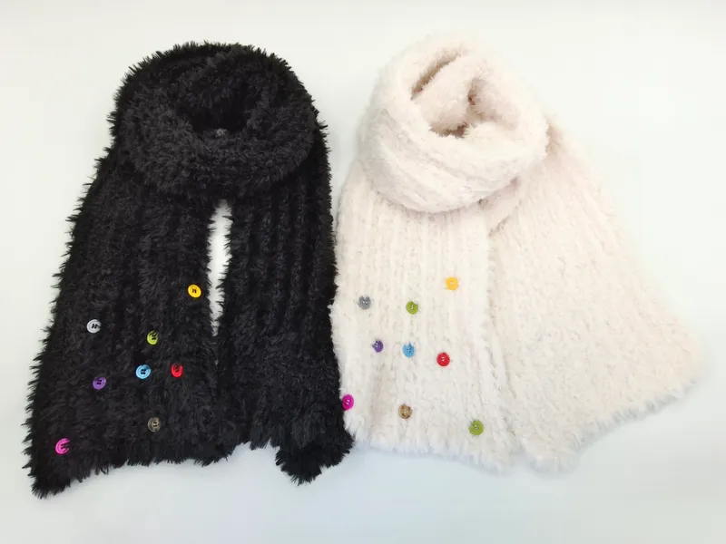 Zwei kuschelweiche Strickschals in Schwarz und Creme mit dekorativen bunten Knöpfen, nebeneinander auf weißem Hintergrund arrangiert