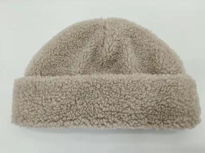 Beigefarbene Sherpa-Fleece-Mütze mit lockig-strukturiertem Stoff und umgeschlagenem Rand, Flachaufnahme auf weißem Hintergrund