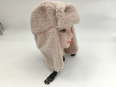 Cremefarbener Sherpa-Ushanka-Trapperhut mit Ohrenschutzklappen und schwarzem Kunststoffschnallen-Kinnriemen auf Hutständer