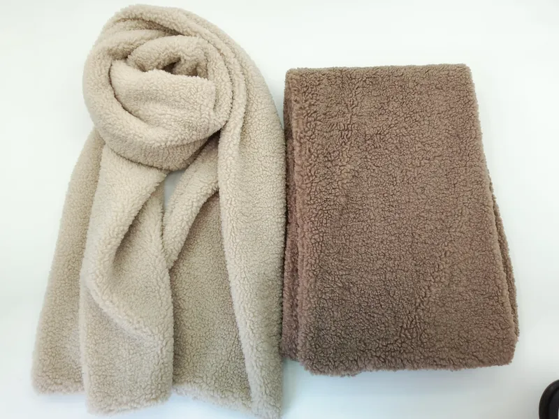 Zwei Sherpa-Fleece-Schals in Beige und Taupe, einer drapiert und einer flach gefaltet, mit sichtbarer Teddybär-Plüschstruktur