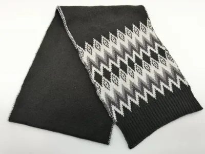 Gefalteter Anthrazit-Strickschal mit weiß-grauem Fair-Isle-Zickzack-Muster und gerippten Abschlussenden, Draufsicht