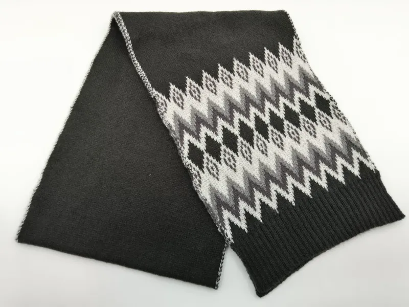 Gefalteter Anthrazit-Strickschal mit weiß-grauem Fair-Isle-Zickzack-Muster und gerippten Abschlussenden, Draufsicht