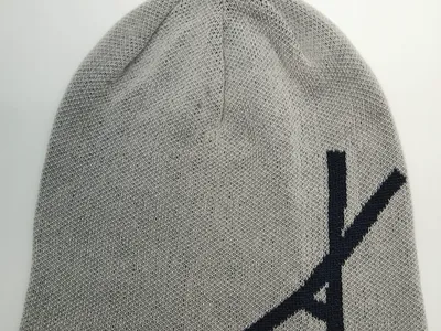 Hellgraue Feinstrick-Slouch-Beanie mit großem navyblauen Schriftzug auf der Vorderseite, Draufsicht auf weißem Untergrund