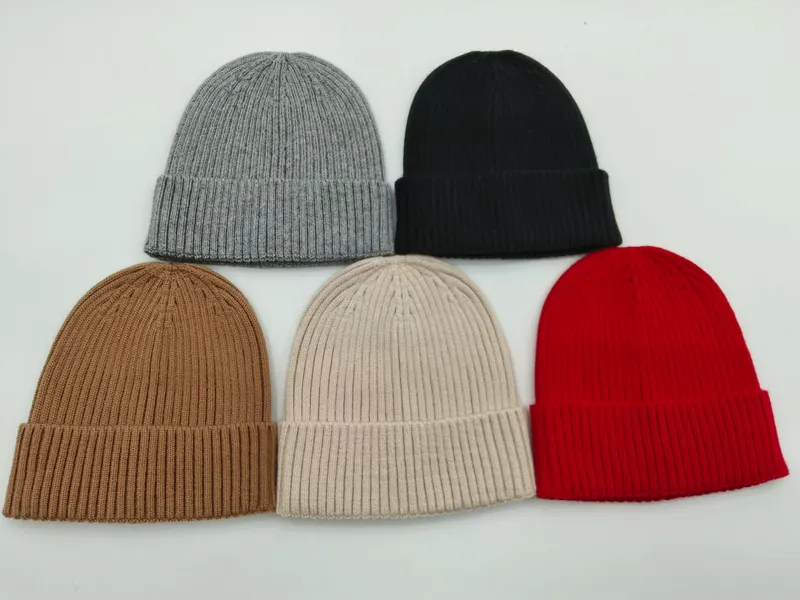 Fünf klassische Rippstrick-Beanies mit Krempenumschlag in den Farbtönen Anthrazit, Schwarz, Kamelbraun, Naturweiß und Weinrot auf hellem Hintergrund