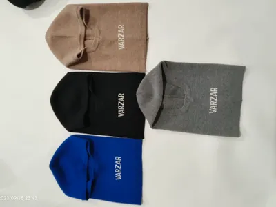 Vier gestrickte Sturmhauben in Beige, Schwarz, Grau und Blau flach auf weißer Fläche, mit besticktem Markenlogo