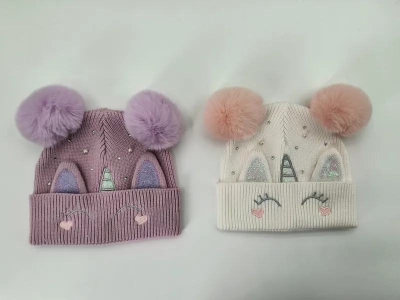 Zwei Einhorn-Beanies für Kinder in Lavendel und Cremeweiß mit flauschigen Doppel-Pompons, Glitzer-Hörnern, bestickten Wimpern und funkelnden Strasssteinen