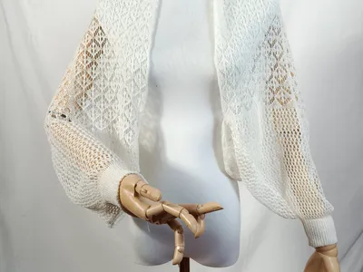 Weißes Häkel-Bolero-Jäckchen mit offenem Schnitt, langen Ballonärmeln und gerippten Bündchen auf einer Schneiderpuppe