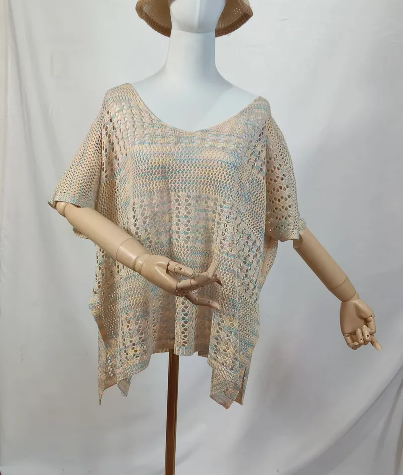 Beigefarbenes Multicolor-Häkelponcho mit Kurzarm auf einer Schneiderpuppe mit Holzarmen, Pastellblau- und Rosatöne sichtbar