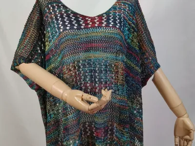 Buntes Boho-Häkelponcho mit Kurzarm auf einer Schneiderpuppe, mit Farbakzenten in Petrol, Rot und Gold