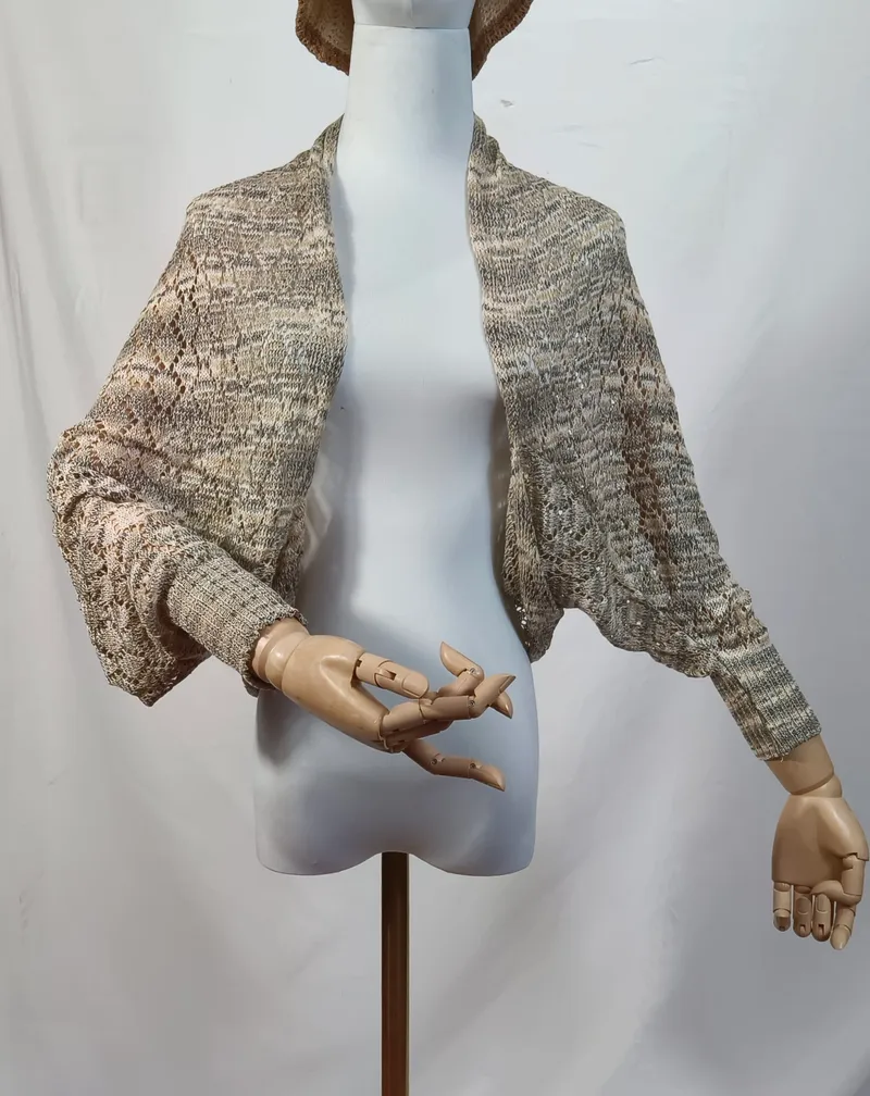 Offenes Spitzenstrick-Shrug in Beige-Grau-Mélange auf einer Schneiderpuppe mit Holzhänden, Fledermausärmel und Rippbündchen sichtbar