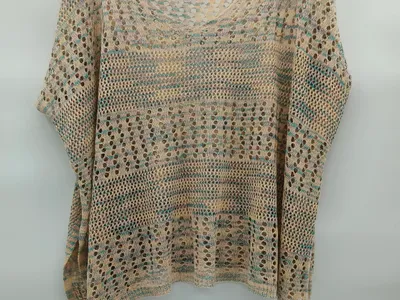 Beige-türkisfarbenes Häkelponcho mit Fledermausärmeln, Streifenmuster und großen Maschen auf einem Kleiderbügel in Studioaufnahme