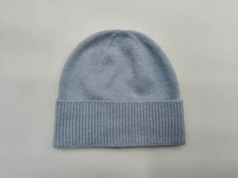 Weiche hellblaue Strickmütze mit breitem umgeklapptem Rippbund, flach auf weißem Hintergrund liegend, nahtloser Mützenabschluss
