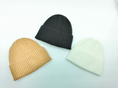 Drei zusammengefaltete Rippstrick-Beanies in Schwarz, Kamel-Braun und Cremeweiß auf weißem Hintergrund, klassischer Umschlagrand
