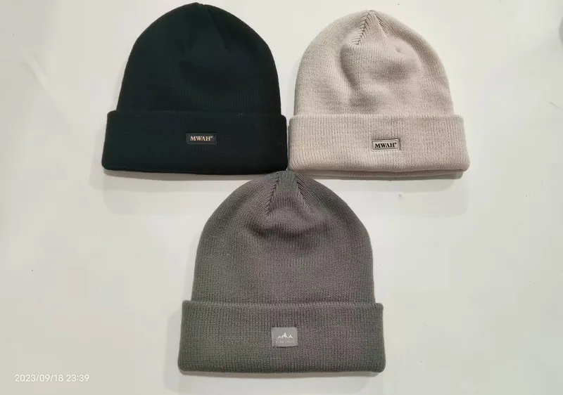 Drei Rippenstrickmützen mit Umschlag flach liegend in Schwarz, Hellbeige und Dunkelgrau, mit kleinen gewebten Markenetiketten am Bund