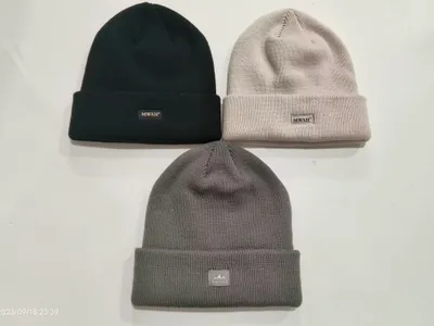 Drei Rippenstrickmützen mit Umschlag flach liegend in Schwarz, Hellbeige und Dunkelgrau, mit kleinen gewebten Markenetiketten am Bund