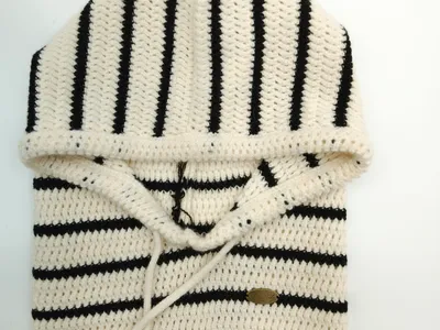 Gefalteter creme-schwarz gestreifter Häkel-Hoodie-Pullover mit Kordelzug-Kapuze und Rippbund, flach auf weißem Hintergrund