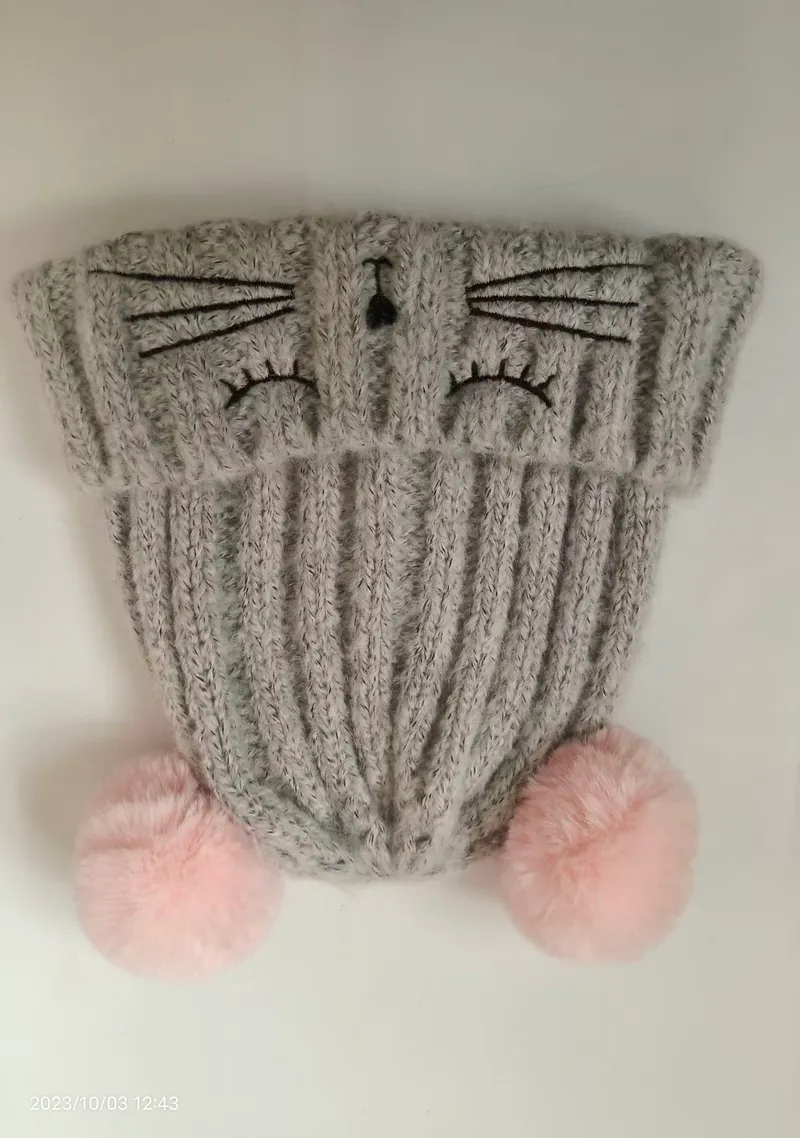 Graue gestrickte Wintermütze mit aufgesticktem Katzengesicht, Schnurrhaaren und zwei pinken Kunstfell-Pompons an der Krempe