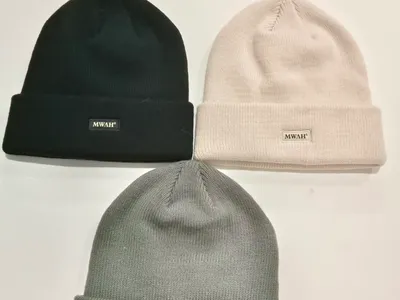 Drei gerippte Strickmützen in Schwarz, Cremeweiß und Grau flach auf weißem Untergrund mit kleinen Markenpatch-Etiketten