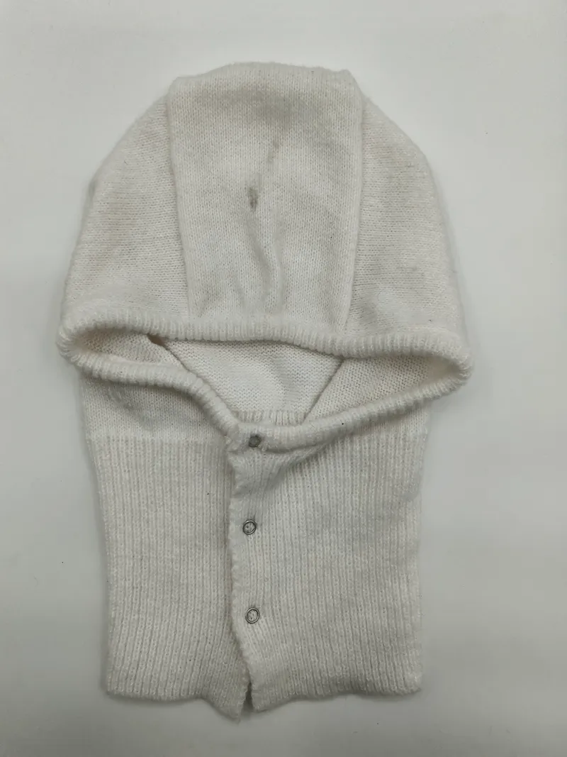 Cremeweiße gestrickte Baby-Helmhaube mit umklappbarer Kapuze und silbernen Druckknöpfen, flach auf weißem Untergrund fotografiert