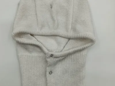 Cremeweiße gestrickte Baby-Helmhaube mit umklappbarer Kapuze und silbernen Druckknöpfen, flach auf weißem Untergrund fotografiert