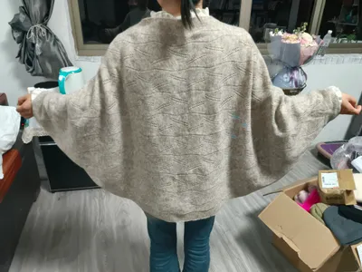 Frau von hinten in übergroßem beigem Fledermausärmel-Pullover mit Rauten-Pointelle-Muster, kombiniert mit blauen Jeans