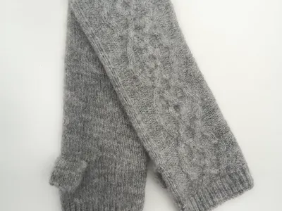 Paar graue fingerlose Handschuhe mit Zopfstrickmuster, Rippenbündchen und Daumenaussparung, flach auf weißem Untergrund