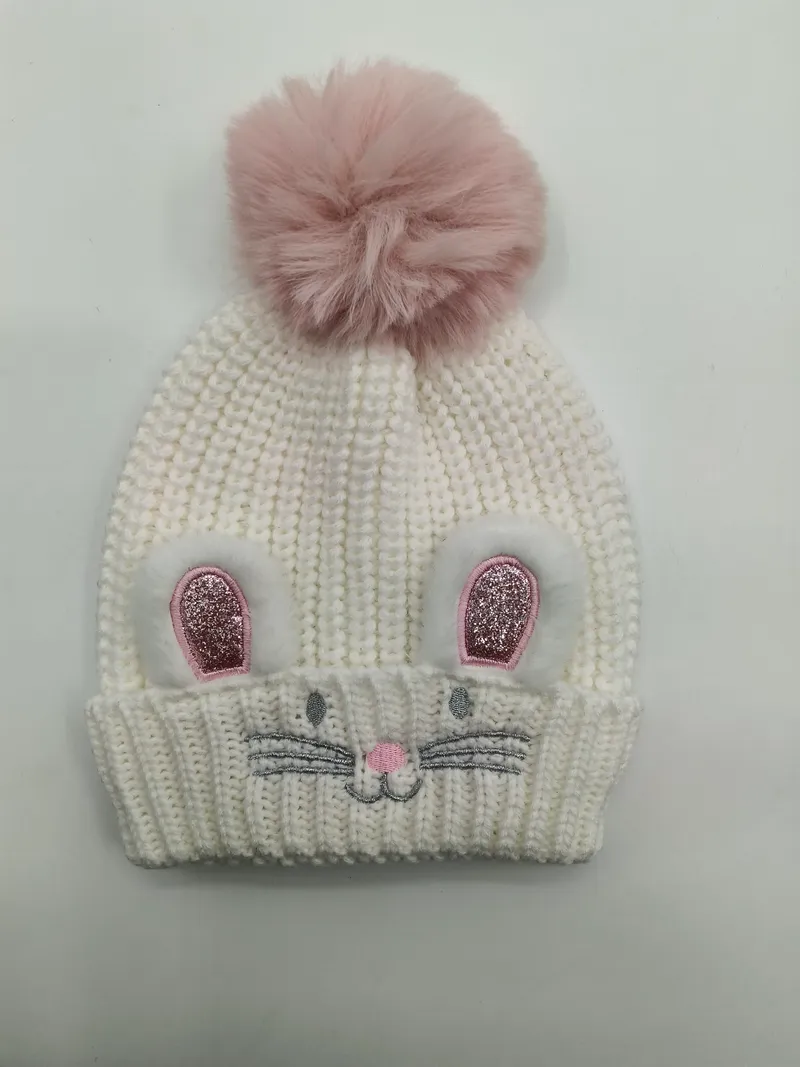 Weiße grob gestrickte Kindermütze mit rosafarbenen Glitzer-Hasenohren, aufgestickten Barthaaren und großem rosa Kunstfell-Bommel oben