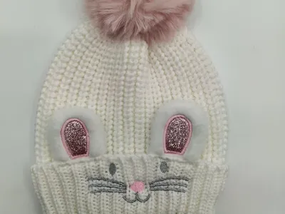 Weiße grob gestrickte Kindermütze mit rosafarbenen Glitzer-Hasenohren, aufgestickten Barthaaren und großem rosa Kunstfell-Bommel oben