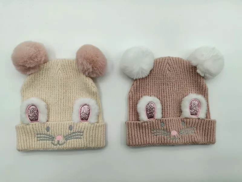 Zwei gerippte Kinderstrickmützen in Creme und Taupe mit flauschigen Doppel-Bommel-Mäuseohren und gesticktem Gesicht nebeneinander