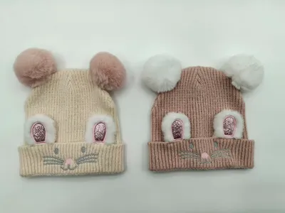 Zwei gerippte Kinderstrickmützen in Creme und Taupe mit flauschigen Doppel-Bommel-Mäuseohren und gesticktem Gesicht nebeneinander