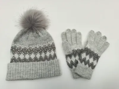 Graue Fair-Isle-Strickmütze mit Kunstfell-Bommel und Perlenapplikationen neben passenden Strickhandschuhen als Set